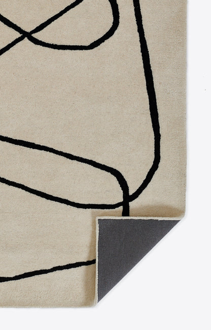 Beige rug with bold black abstract line drawing; fabric corner folded to show gray underside.