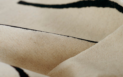 Beige rug with black curved stripes, soft texture and visible folds.