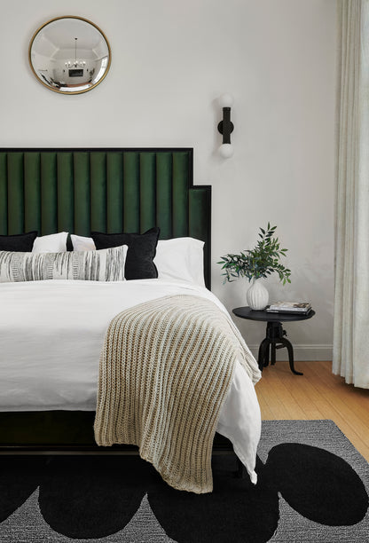 Rug (2' x 3') in a bedroom setting: green vertical headboard with black frame, white bedding, beige chunky knit throw; round gold mirror and black sconce.