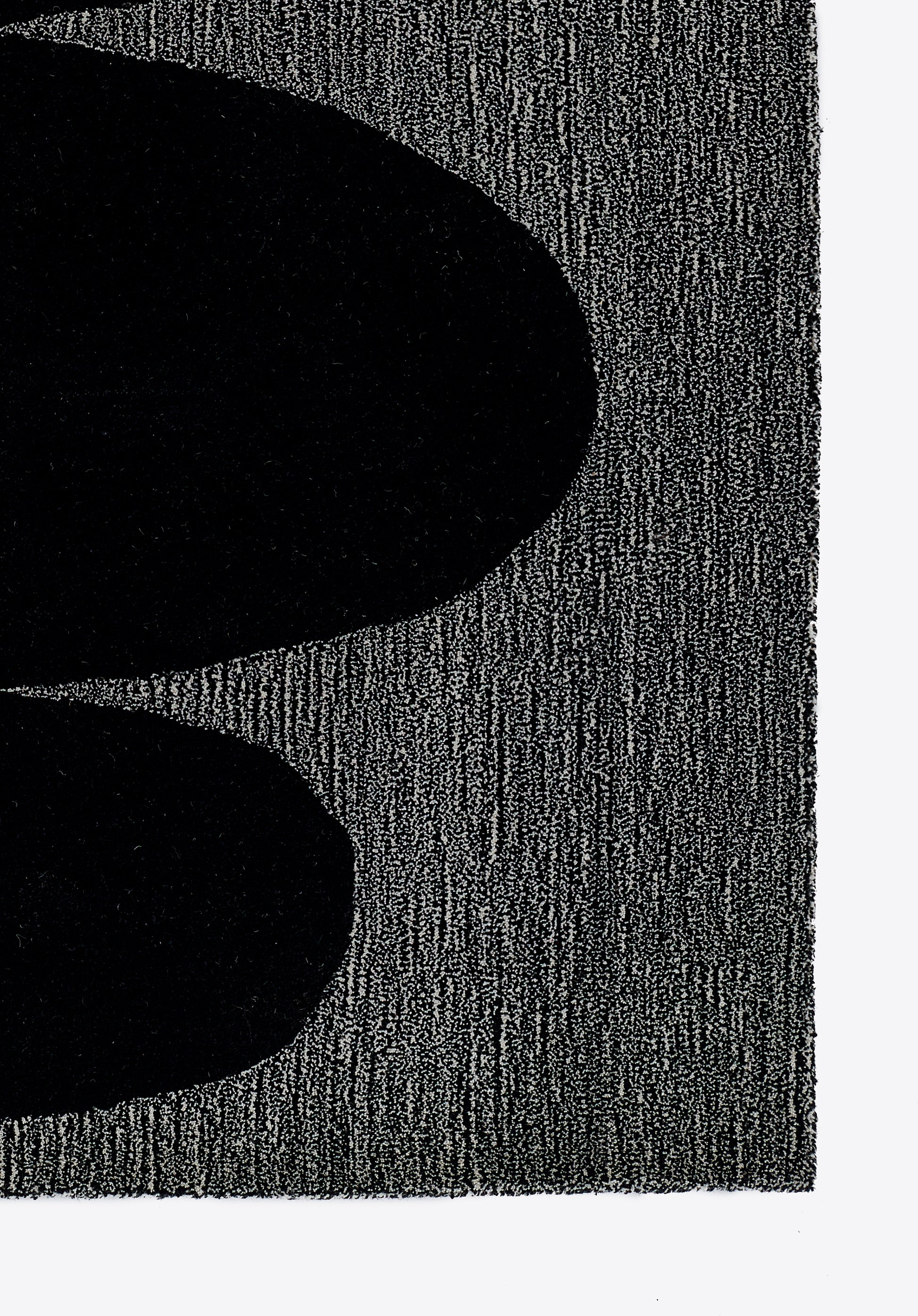 Close-up of two large black ovals on a textured dark gray rug; bold, abstract minimalist design.