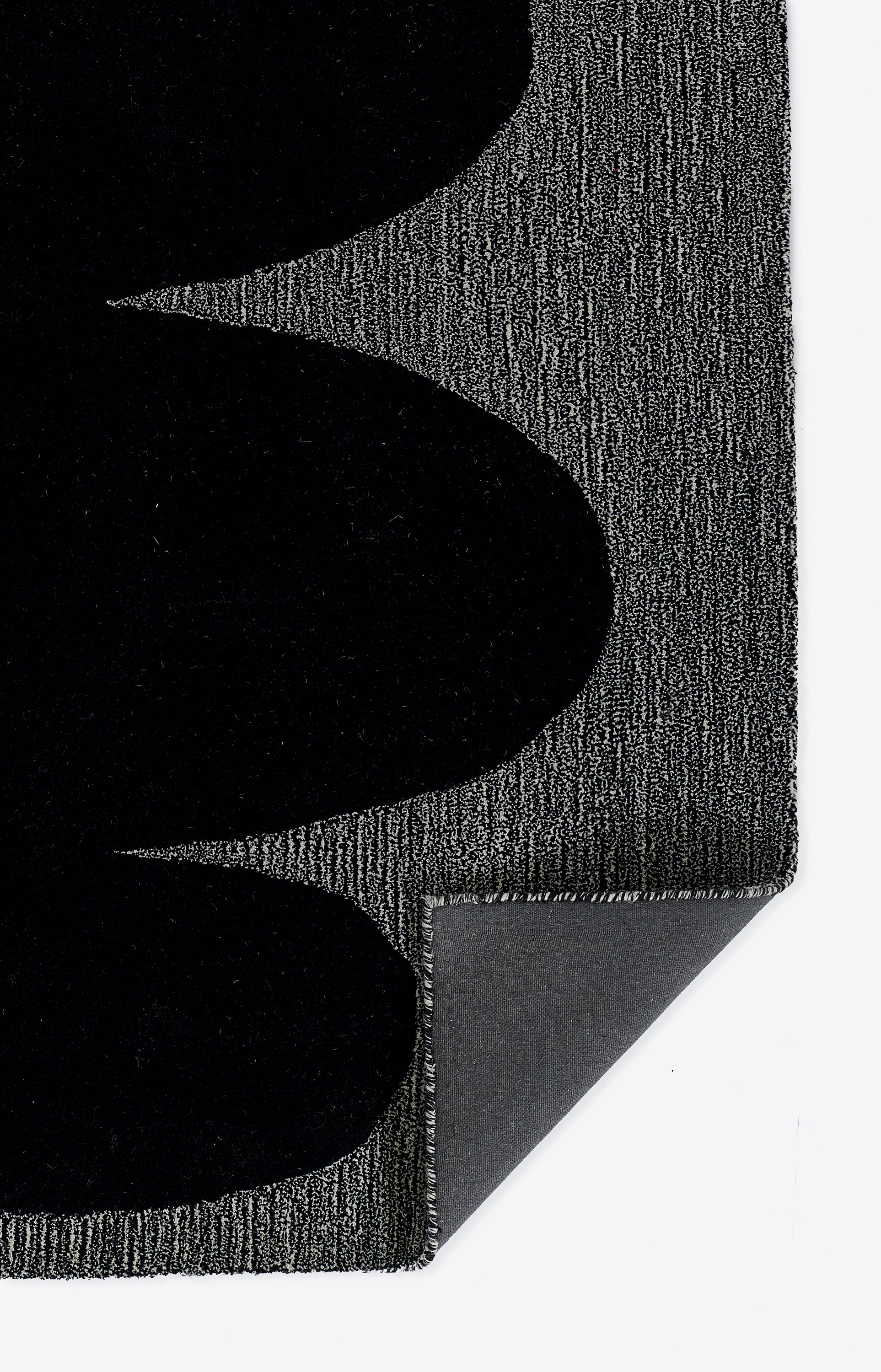 Close-up of a black textured rug with curved black shapes on a gray woven background; corner folded to reveal underside.