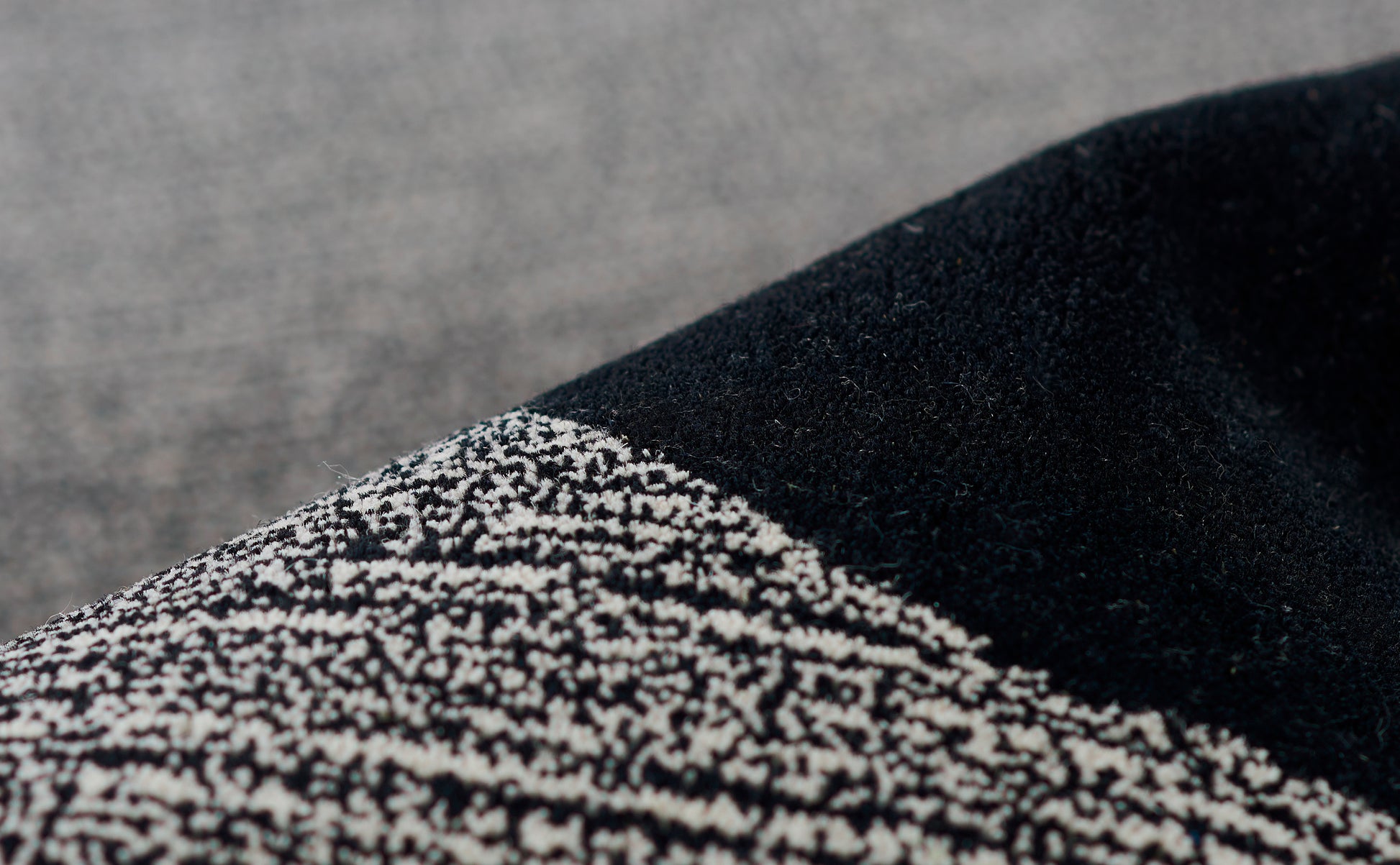 Close-up of black rug fibers beside beige-black speckled tweed, showing textured weave and seam.