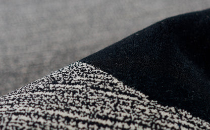 Close-up of a black rug with a speckled black-and-white tweed panel and a diagonal seam.