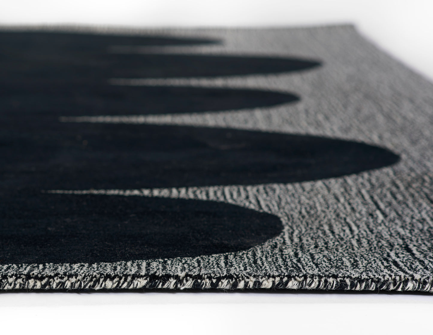 Charcoal black rug with dense loop-pile texture, subtle pattern, and light edge fringe; close-up shot.