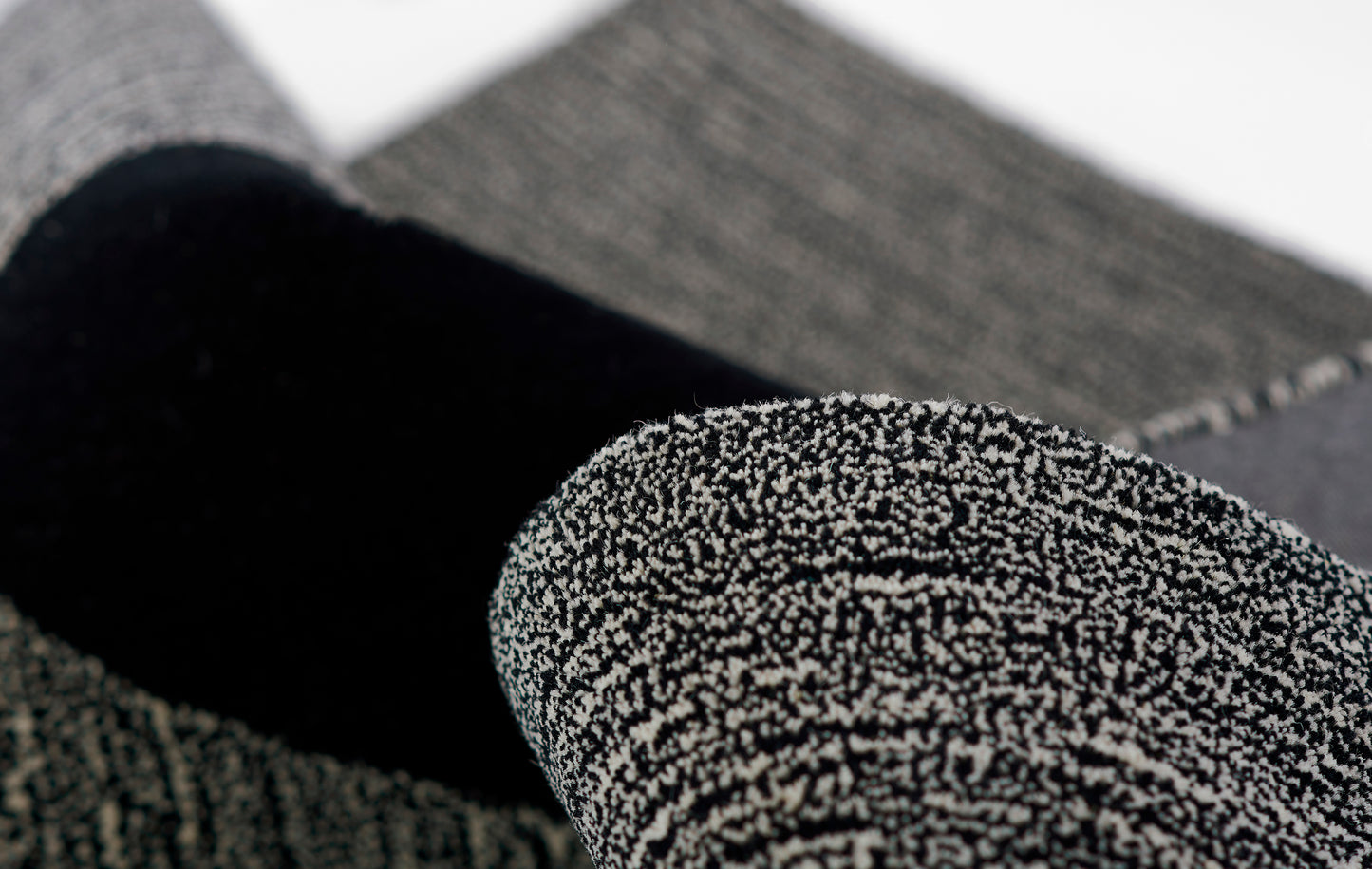 Close-up of a rolled black boucle-knit rug with gray specks.