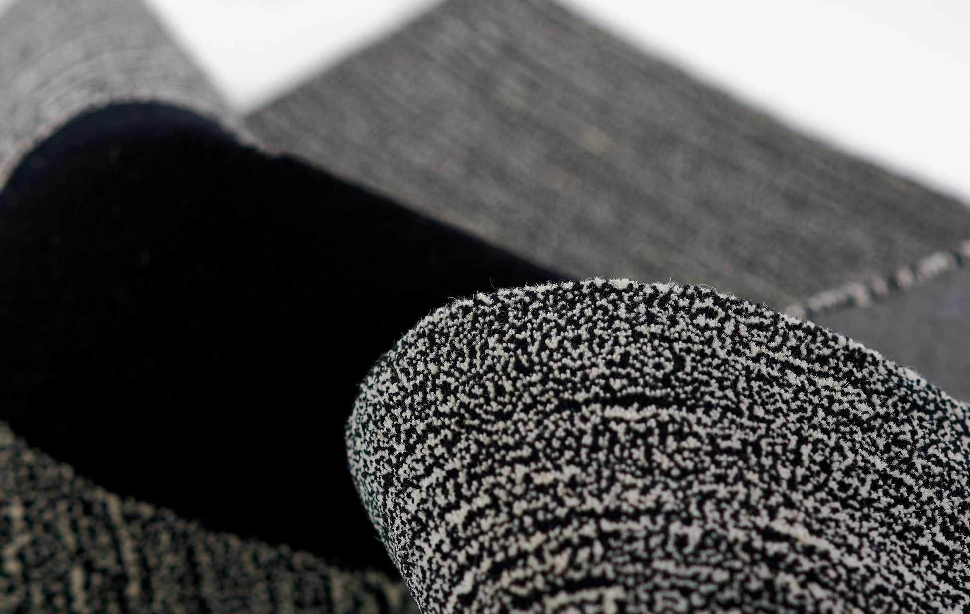 Close-up of a rolled black boucle-knit rug with gray specks.
