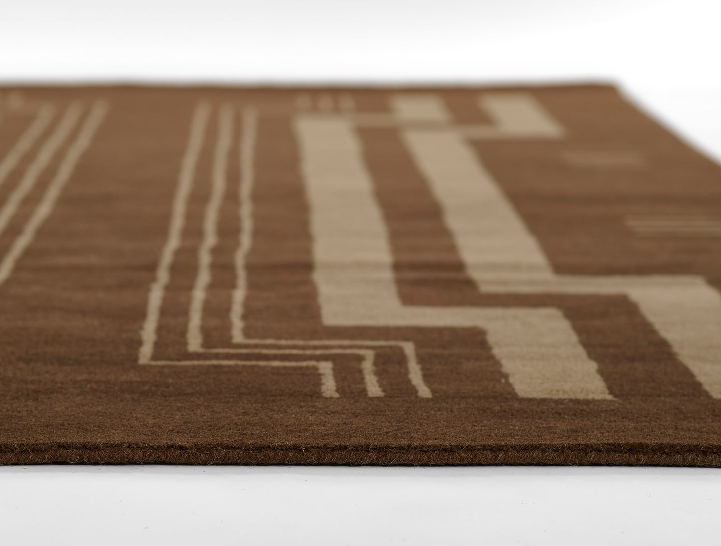 Brown rug with beige geometric line pattern, close-up edge view.