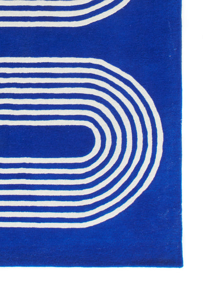 Blue rug with white concentric curved stripes forming a rounded loop; modern geometric design.
