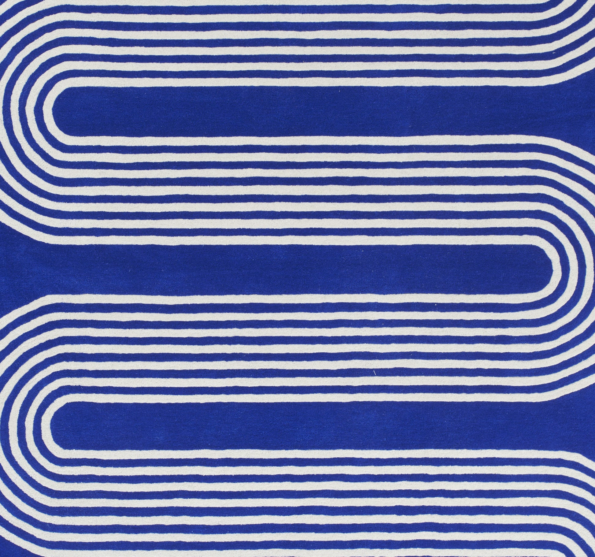 Blue rug with white curved stripes forming a looping retro geometric pattern.