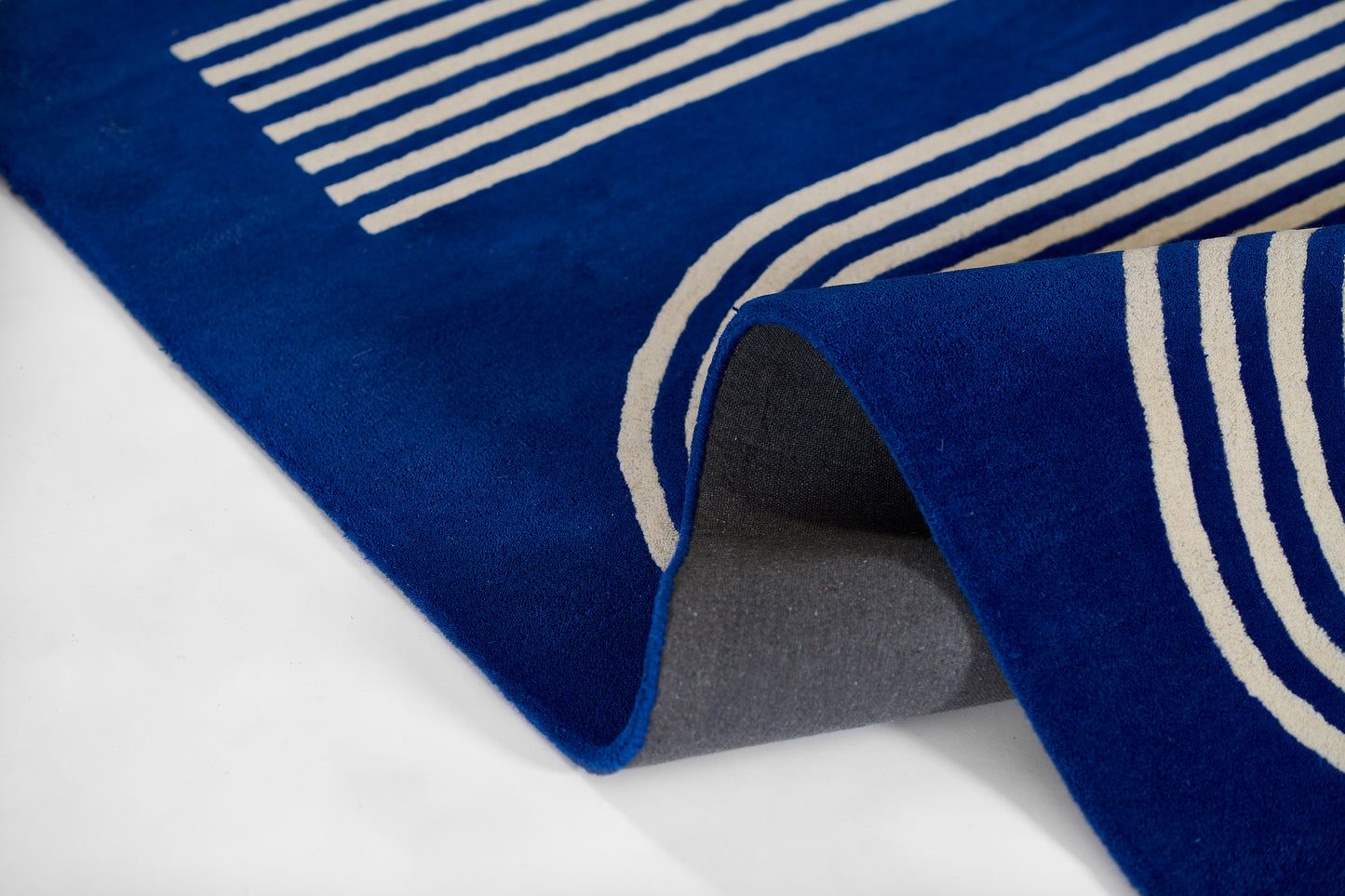 Blue rug with white geometric stripes, folded to show gray backing.