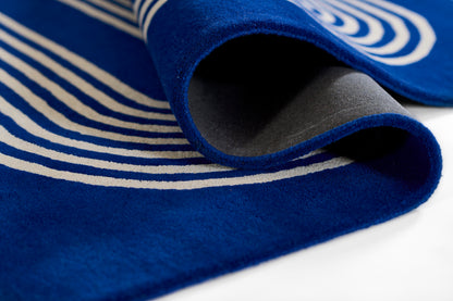 Blue rug with white stripes, folded corner, soft pile; size 2' x 3'.