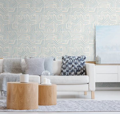 Modern living room with white sofa, pale blue geometric wallpaper, round wood coffee tables, gray cushions, pastel artwork.