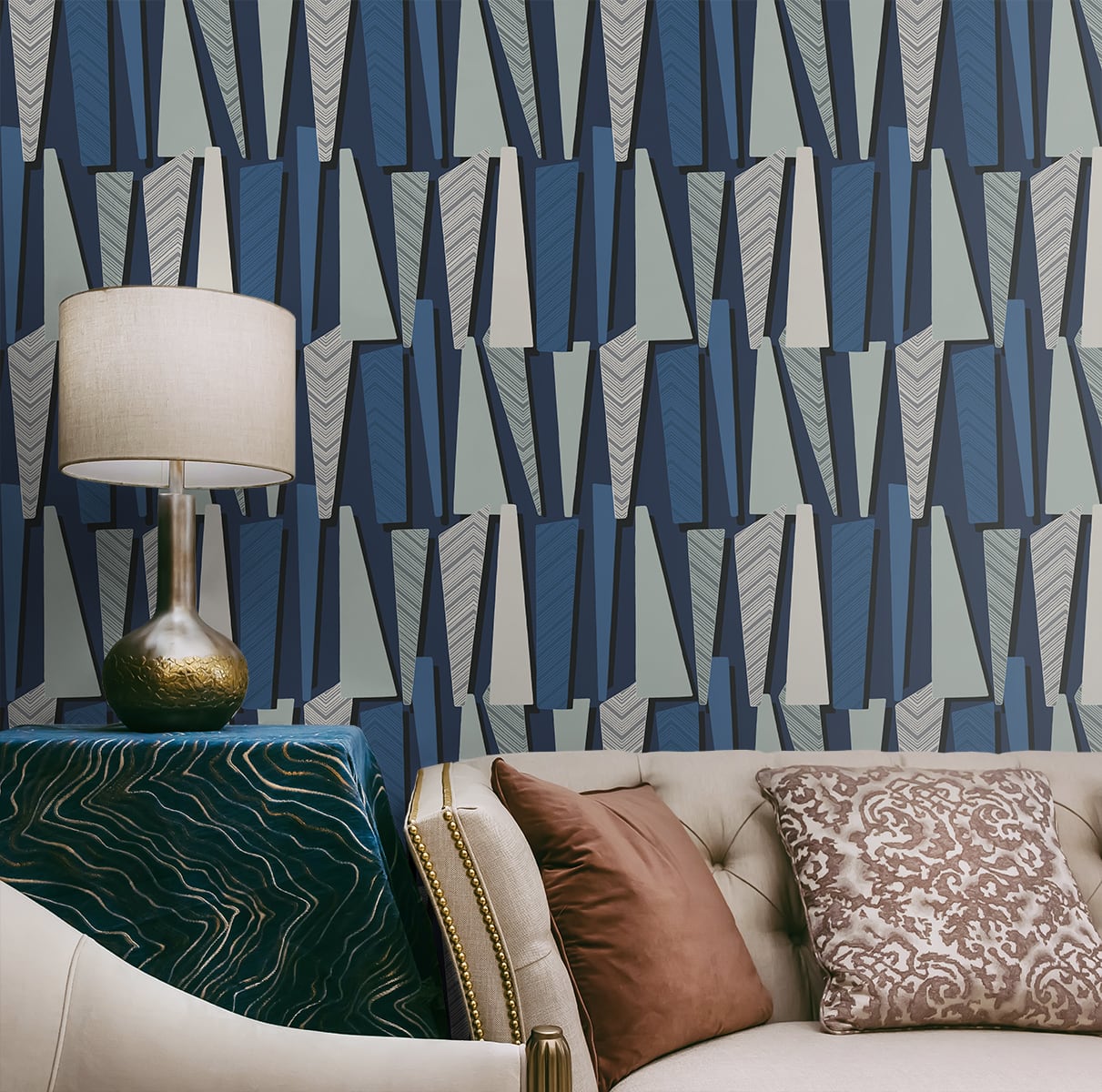 Geometric navy & gray wallpaper; beige tufted sofa, brown damask cushions; brass lamp, cream shade, green velvet table.