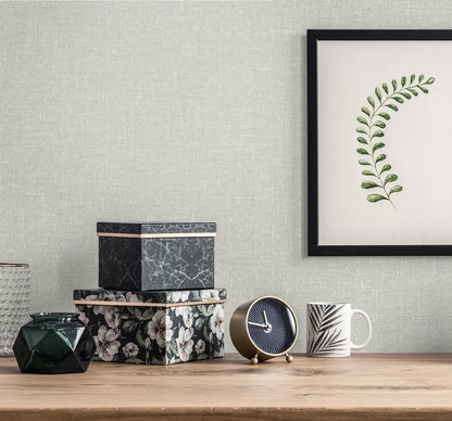 Flat lay with soft grey linen background featuring a stack of black floral and marble boxes, brass clock, faceted dark vase, striped mug, and a framed botanical print on a gray wall.