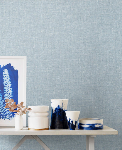 Blue linen fabric on a light wood table with framed blue art and dried flowers.