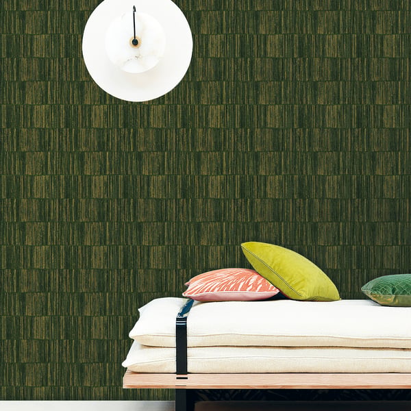 Stack of beige blankets with peach, yellow and teal pillows against a dark green textured wall; white circular clock overhead.