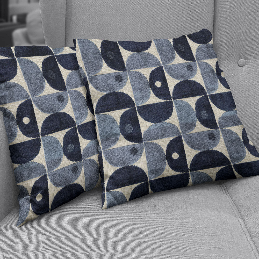 Two square decorative pillows with a navy-blue and light-blue circular geometric pattern on cream-beige fabric, on a grey sofa.