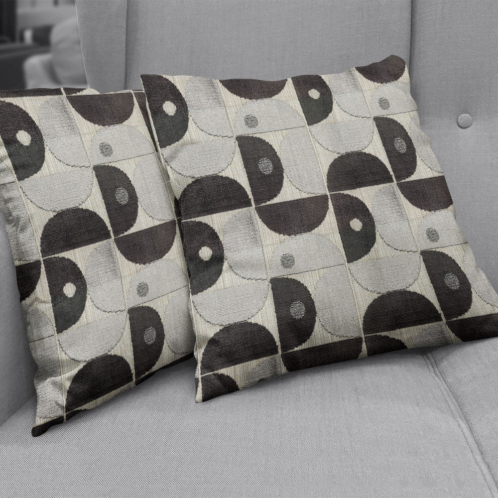 Two rectangular throw pillows in carbon velvet with a black and gray geometric half-circle pattern on a gray sofa.