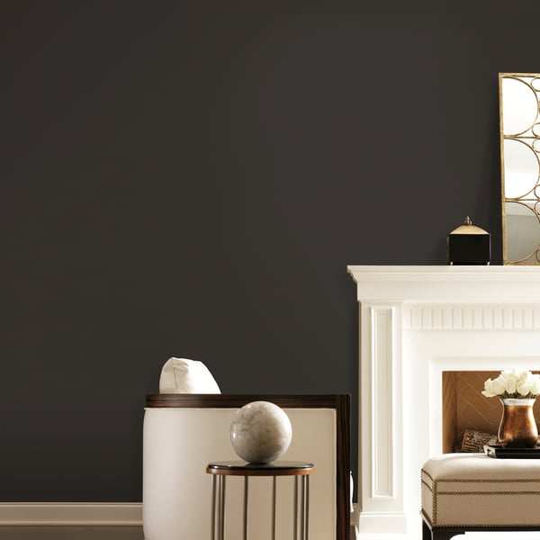 Charcoal wallpapered wall with white mantel fireplace; round marble globe on a small copper-legged side table; beige tufted ottoman.