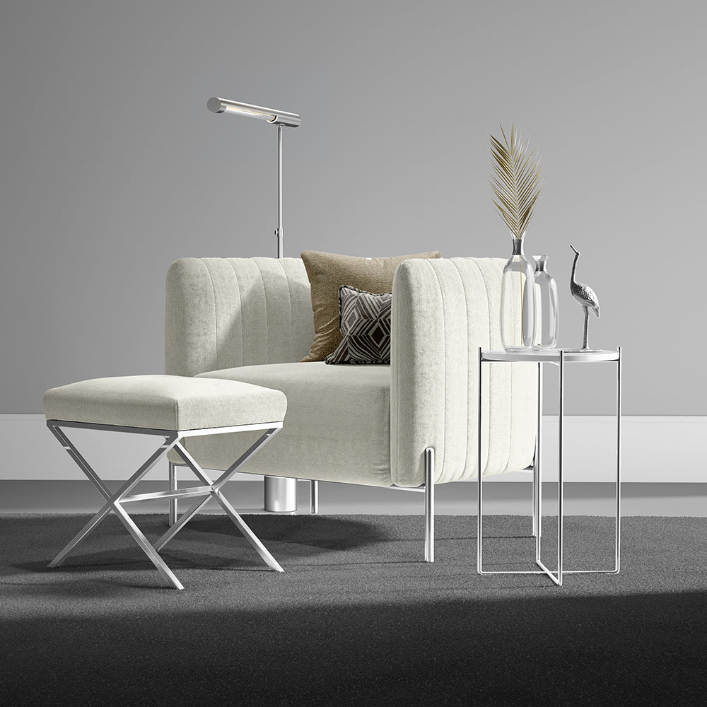 Ivory solid fabric club chair with matching ottoman and chrome legs; glass side tables with decanters and a palm leaf arrangement.