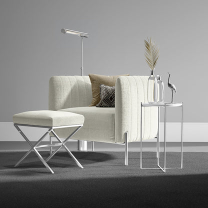 Ivory solid fabric club chair with matching ottoman and chrome legs; glass side tables with decanters and a palm leaf arrangement.