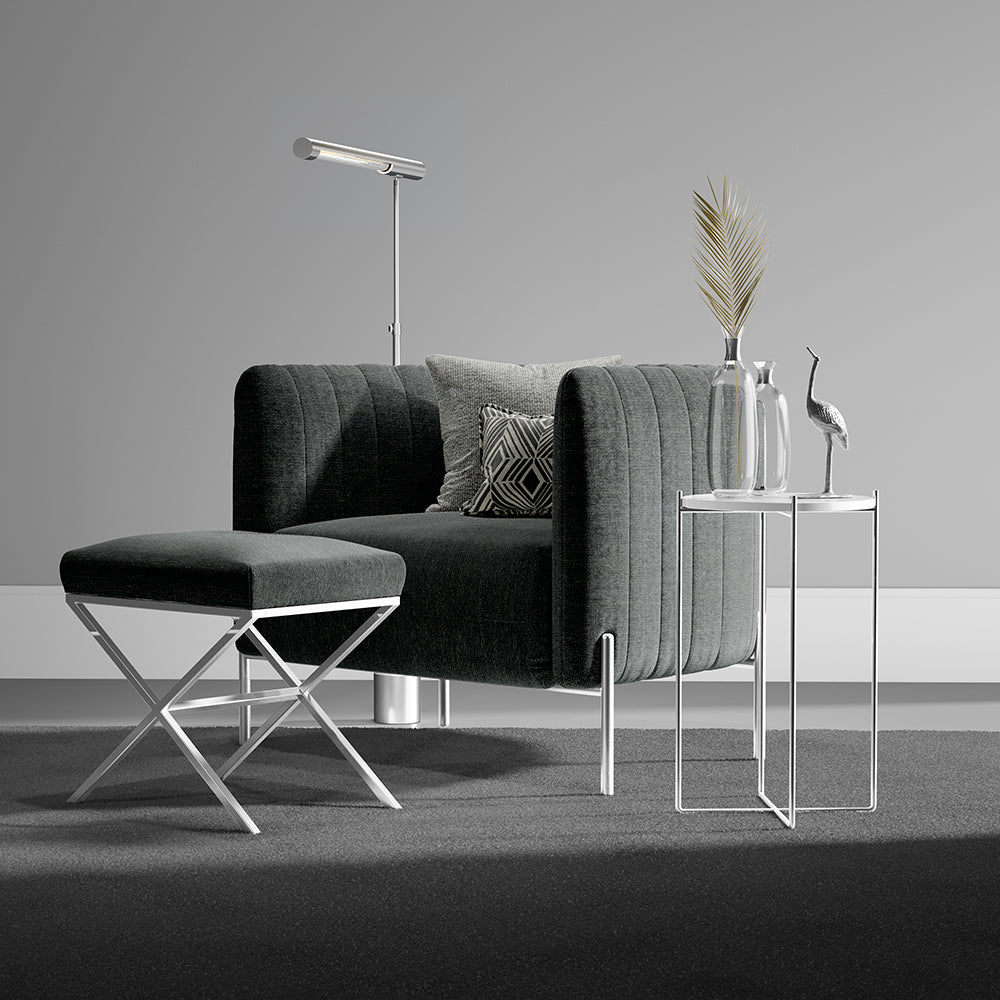 Dark gray upholstered sofa with matching ottoman, chrome legs, floor lamp, and glass-top side tables with vases.