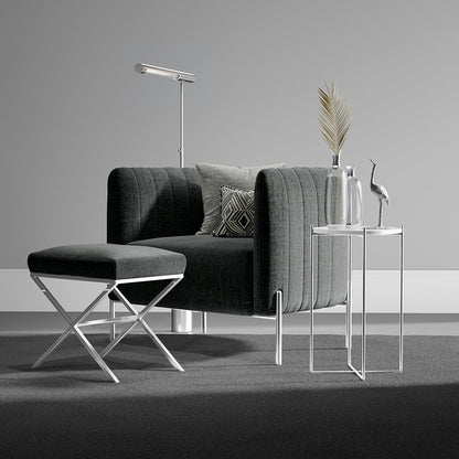 Dark gray upholstered sofa with matching ottoman, chrome legs, floor lamp, and glass-top side tables with vases.