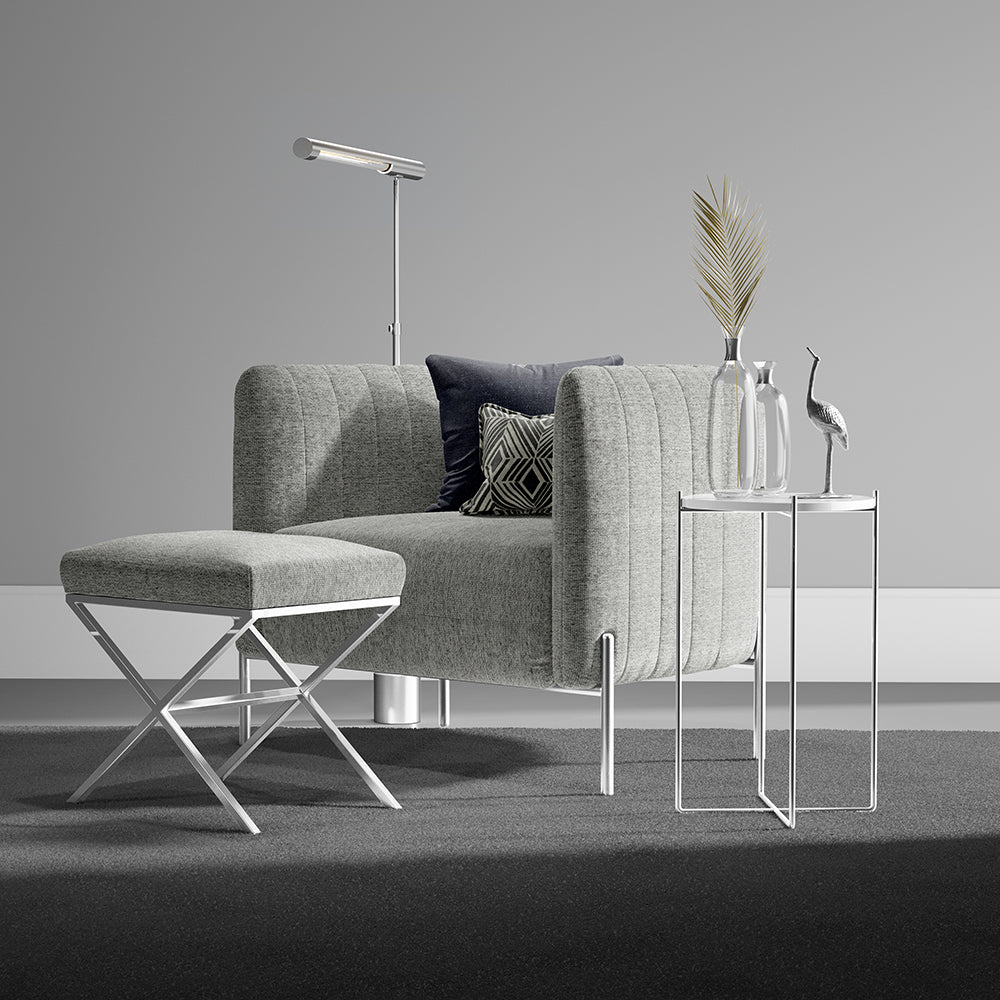 Grey solid fabric upholstery on an armchair with a matching ottoman; dark navy and geometric cushions; chrome legs; glass side tables; modern decor.