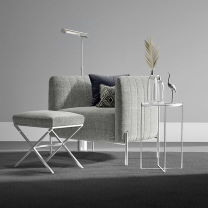 Grey solid fabric upholstery on an armchair with a matching ottoman; dark navy and geometric cushions; chrome legs; glass side tables; modern decor.