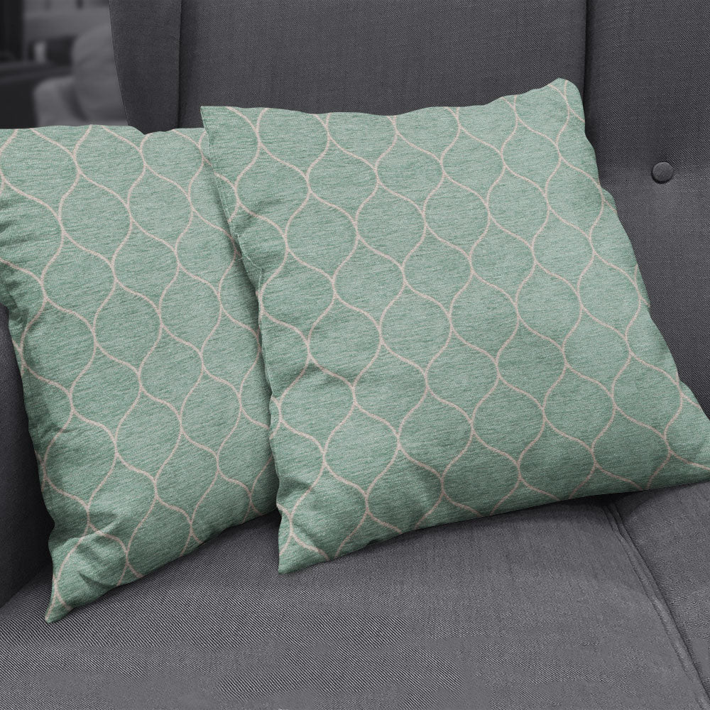 Teal-green square cushions with white geometric lattice pattern on a gray tufted sofa.