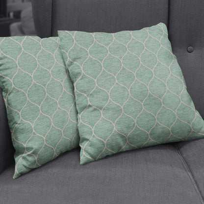 Teal-green square cushions with white geometric lattice pattern on a gray tufted sofa.