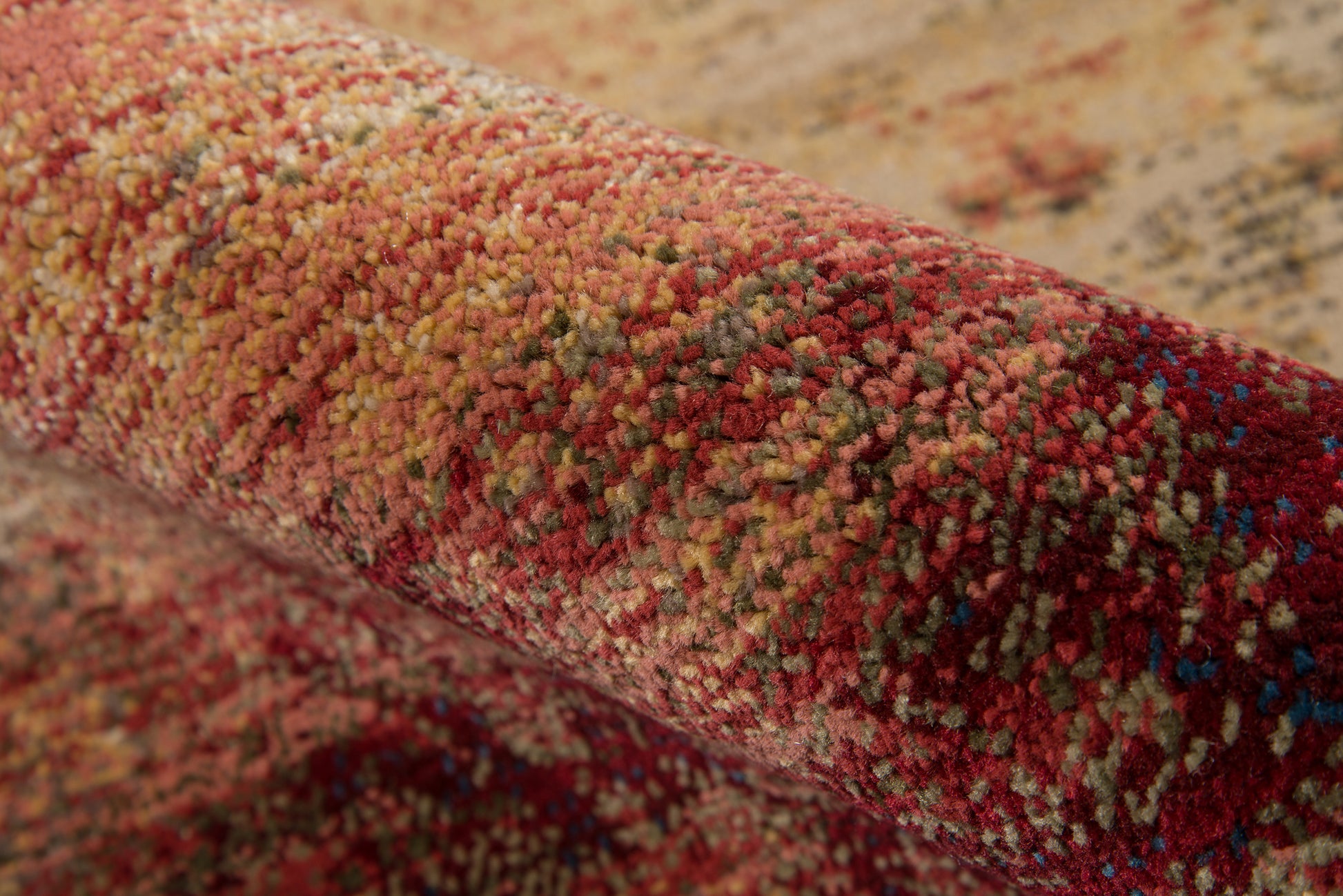 Rolled plush rug with red base & beige, green & yellow flecks; dense textured pile, warm living-room accent.