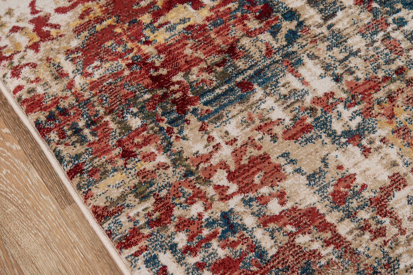 Distressed multicolor area rug with red, blue, beige and yellow tones on hardwood floor; beige edge binding.