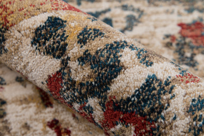 Beige plush oriental rug with blue, red and mustard geometric motifs, partially rolled.