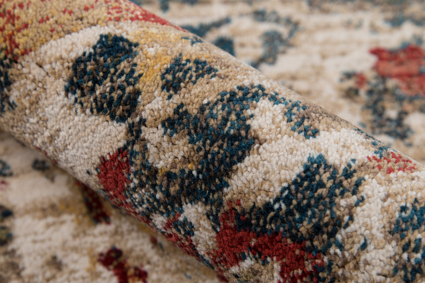 Beige geometric rug with blue and red accents, plush tufted pile, rolled edge revealing dense texture.