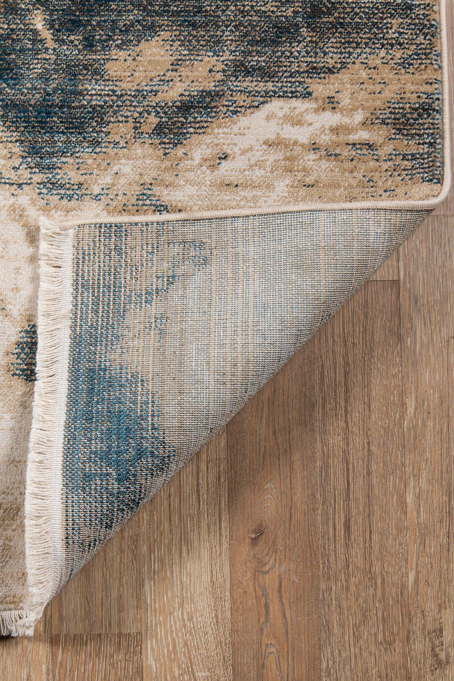 Abstract blue and beige rug with fringe, folded corner shows blue underside on wood floor.