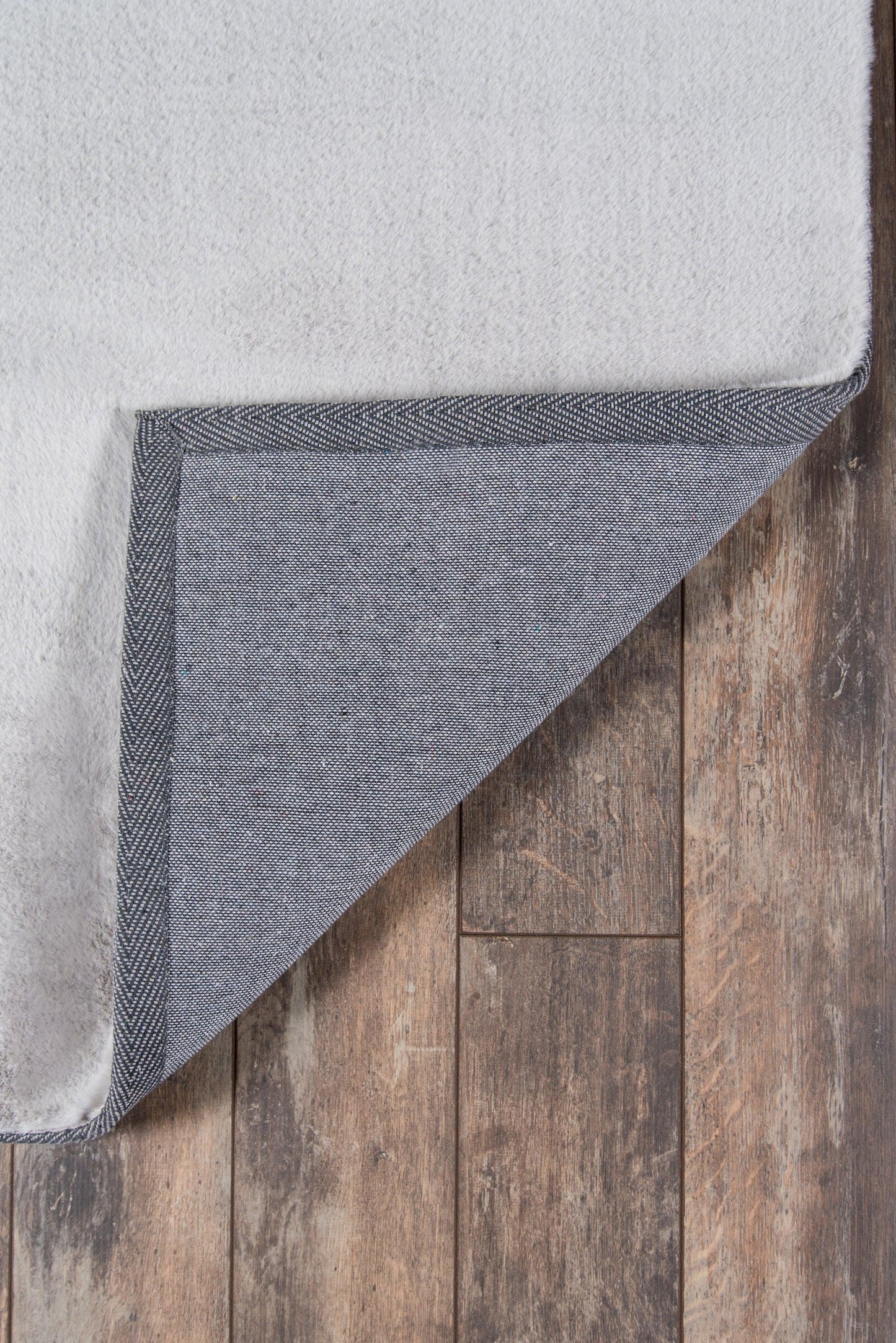 Light gray plush rug with blue denim underside and dark bound edge, folded corner on wood floor.