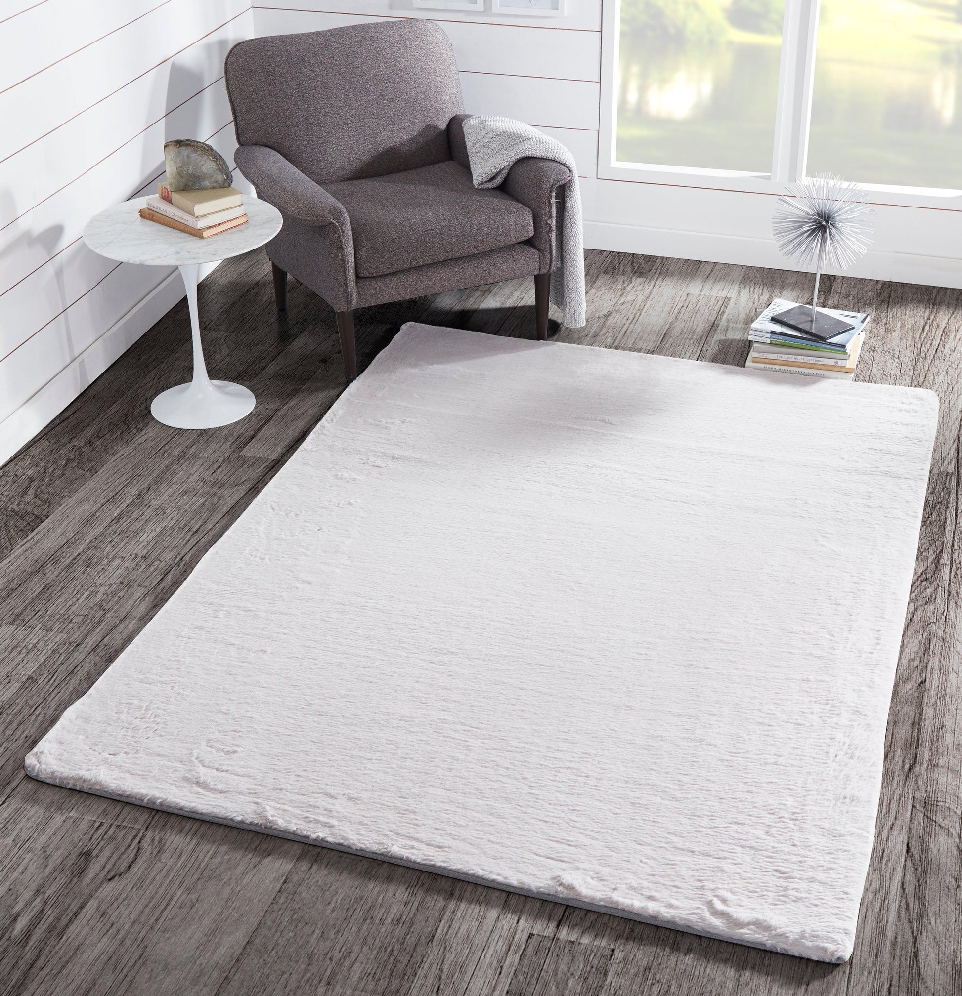 Soft cream rectangular shag rug on wood floor beside a gray upholstered armchair in a cozy modern living room.