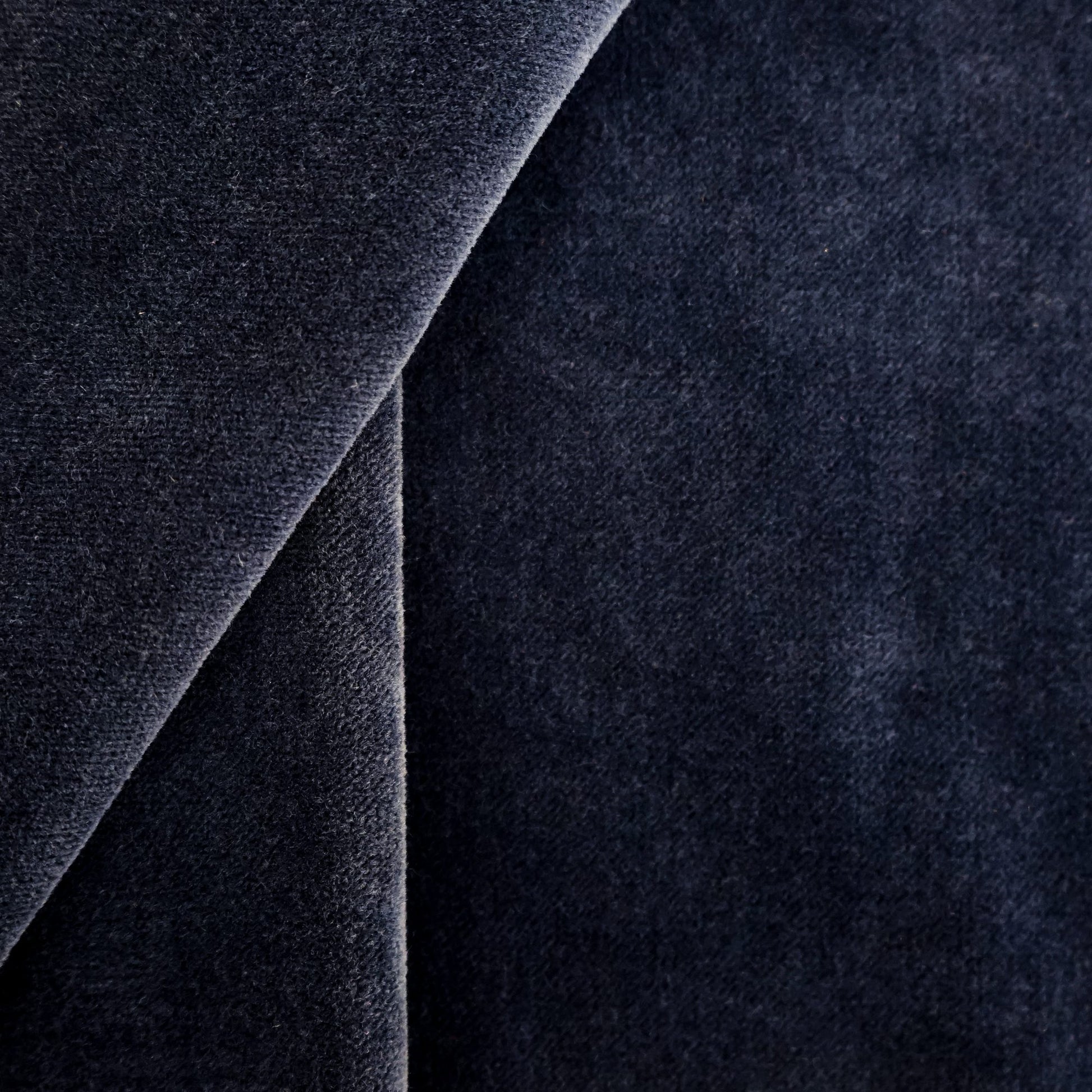 Close-up of dark navy velvet fabric with a diagonal fold, showcasing rich plush texture.