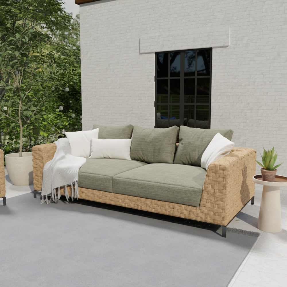 Outdoor wicker sofa with olive cushions, beige woven frame, white and olive pillows on a sunlit patio.