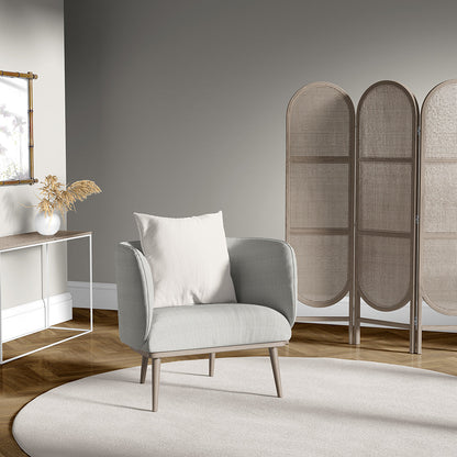 Light gray upholstered mid-century armchair with pale cushion on a round beige rug beside a three-panel woven screen.