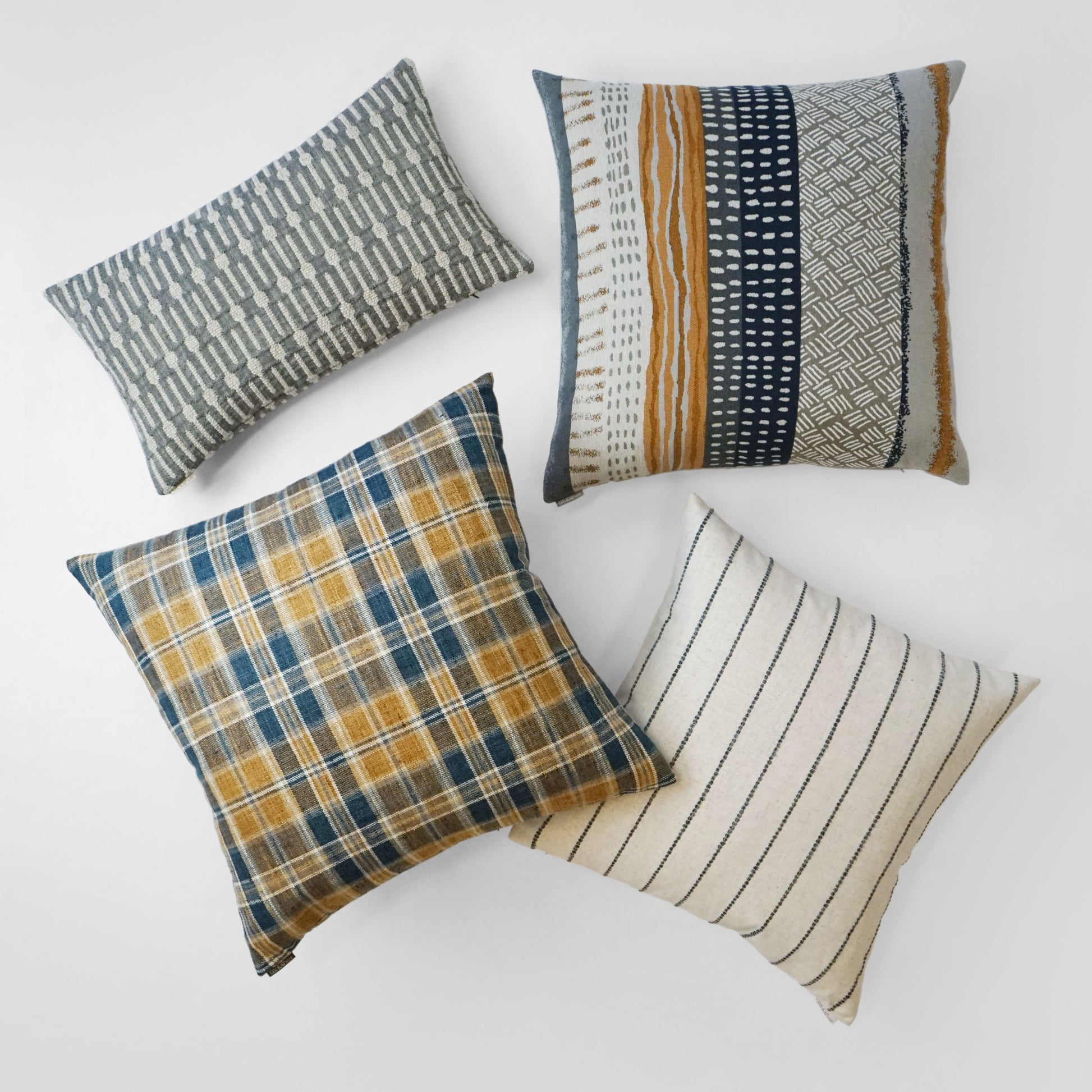 A 24" x 24" rectangular decorative throw pillow with plaid, striped and geometric patterns in navy, mustard, gray and cream.