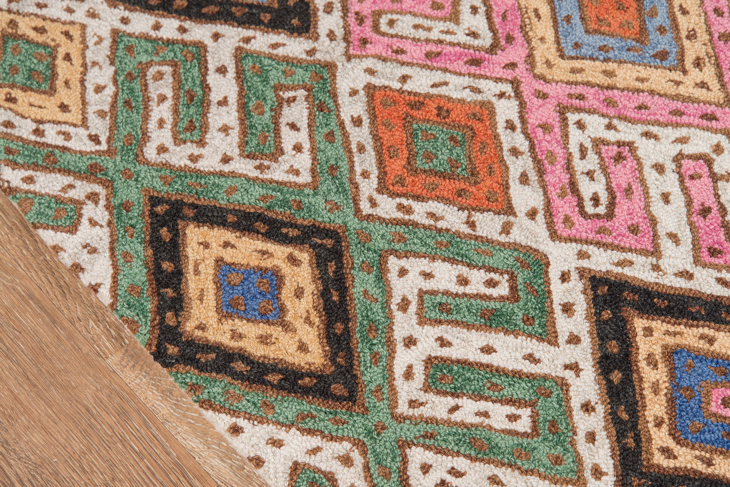 Colorful geometric rug with Greek-key motifs in green, pink, orange, blue and beige on cream, edged by a wood floor.