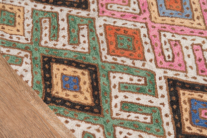 Colorful geometric runner with Greek-key squares in green, pink, orange, blue on beige background; wood floor corner.