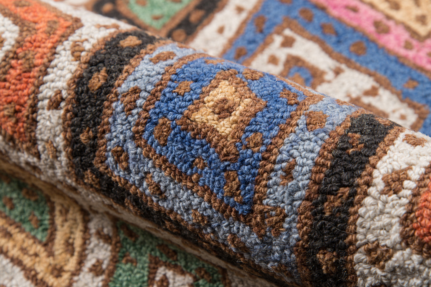 Rolled multicolor woven rug with blue, brown, tan, cream geometric medallion pattern & plush tufted pile.