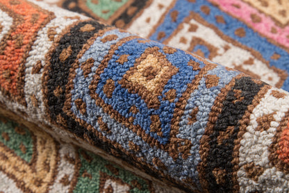 Rolled multicolor woven rug with blue, brown, tan, cream geometric medallion pattern & plush tufted pile.