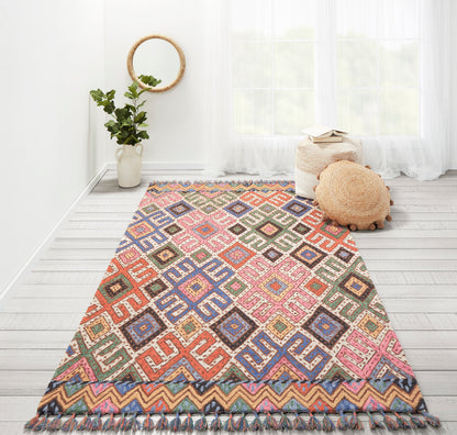 Colorful geometric diamond rug with multicolor squares and fringe, on a whitewashed floor in a bright airy room.