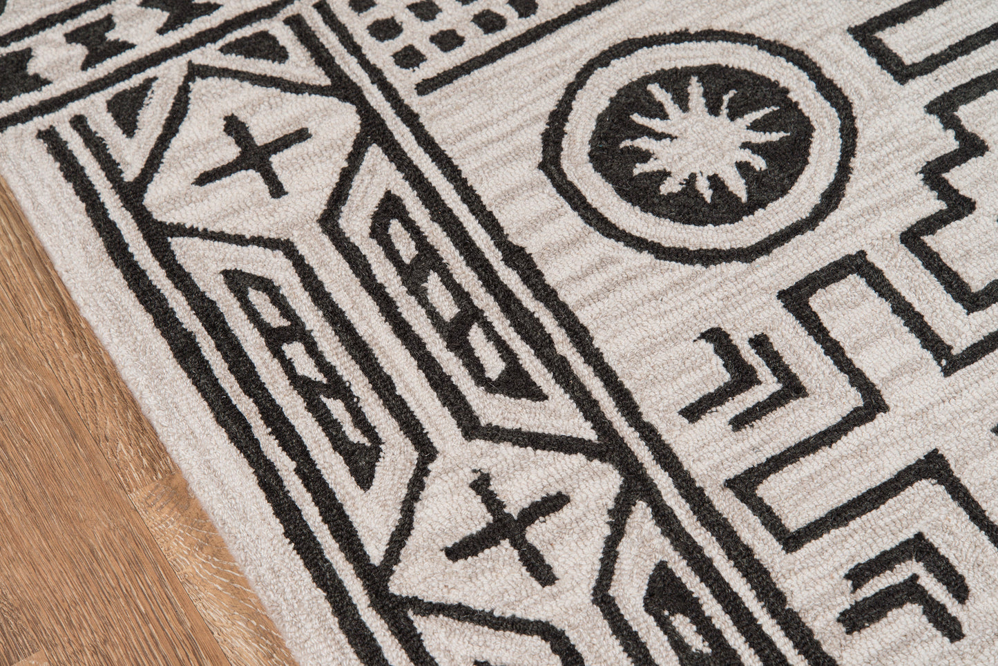 Rectangular ivory rug with bold black geometric tribal pattern, fringed edges, woven texture on wood floor.