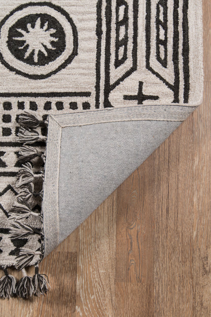 Cream and black geometric rug with fringe tassels; folded corner shows light denim-backed underside on wood floor.