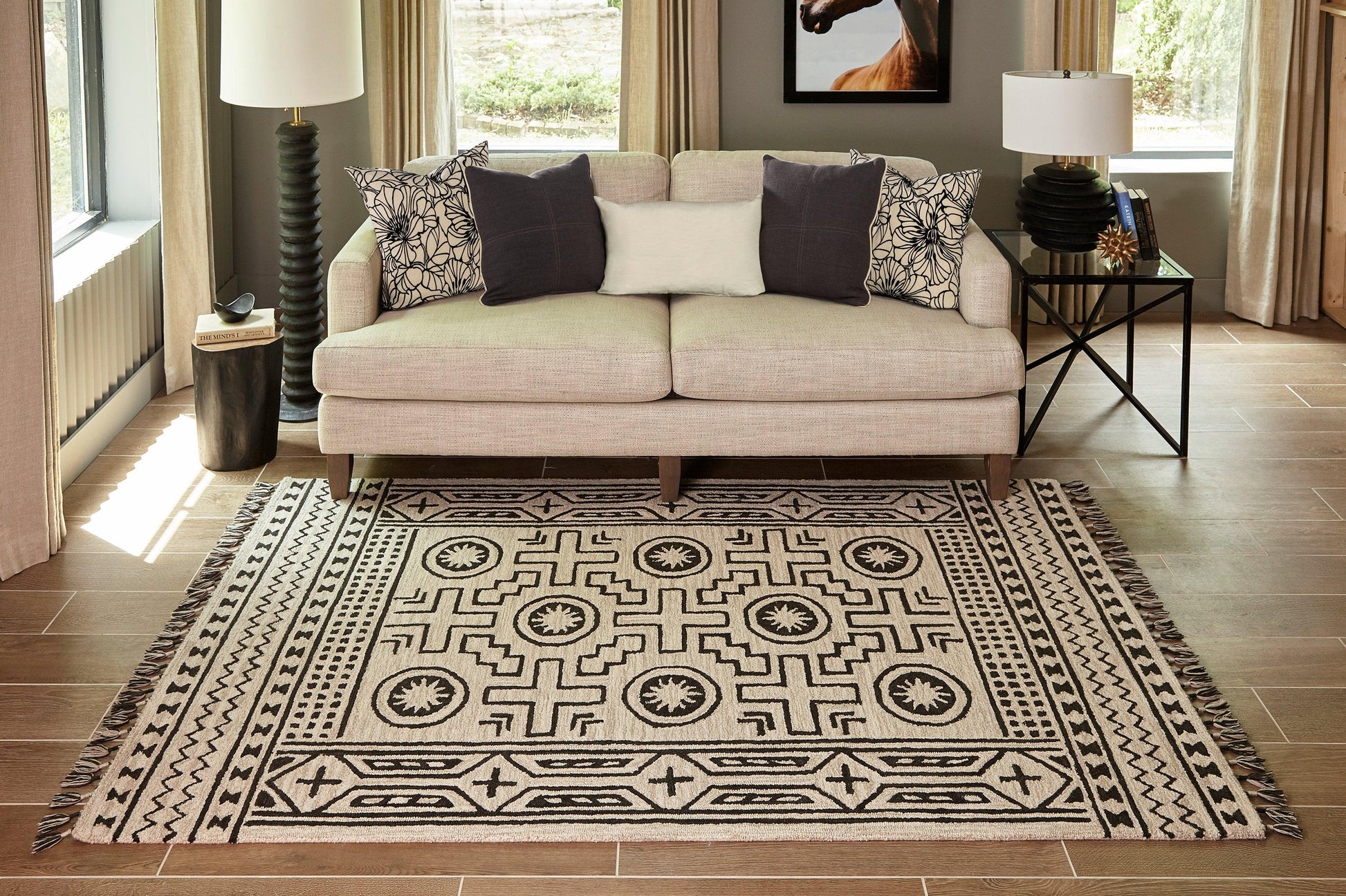 Beige fabric sofa with black and white patterned cushions sits on a rectangular geometric area rug with fringe.